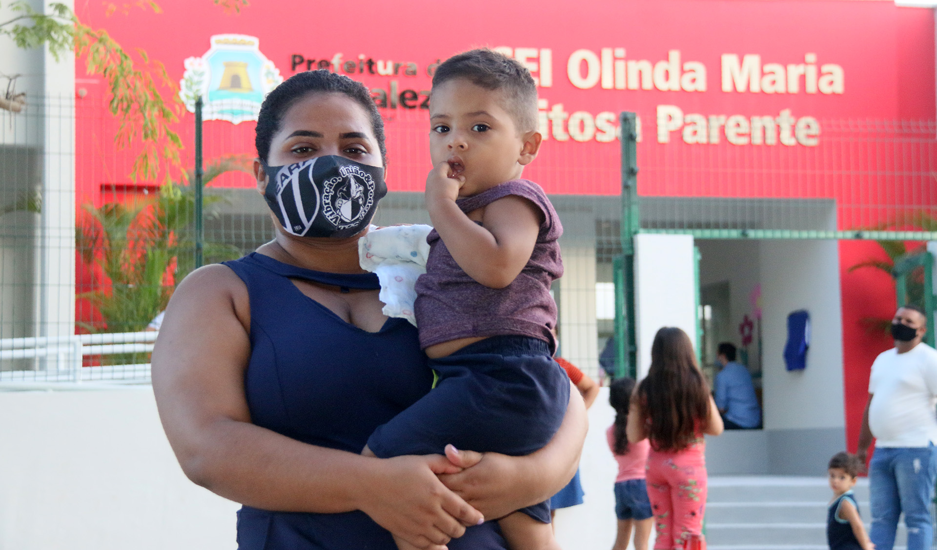 mulher, com máscara, segura, criança no colo enquanto posa para a foto